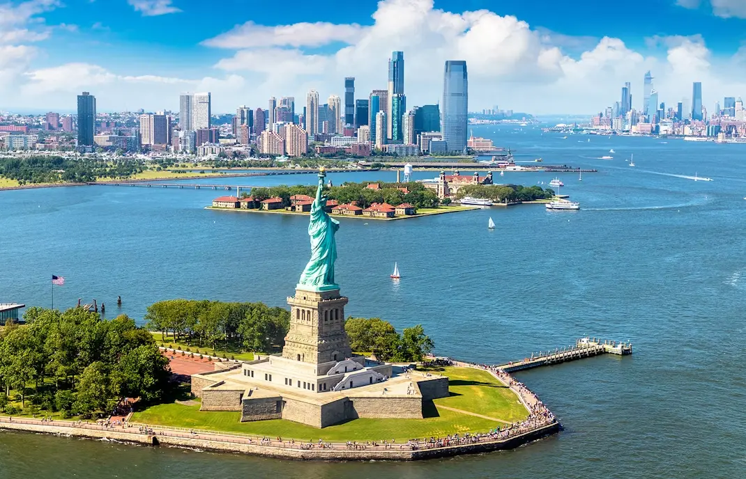 Estátua da Liberdade com skyline da cidade ao fundo sob céu azul